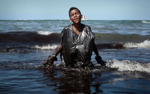 A boy walks out of the sea while removing oil spilled on Itapuama beach located in the city of Cabo de Santo Agostinho, Pernambuco state, Brazil, on October 21, 201 - Credit: &nbsp;LEO MALAFAIA/&nbsp;AFP