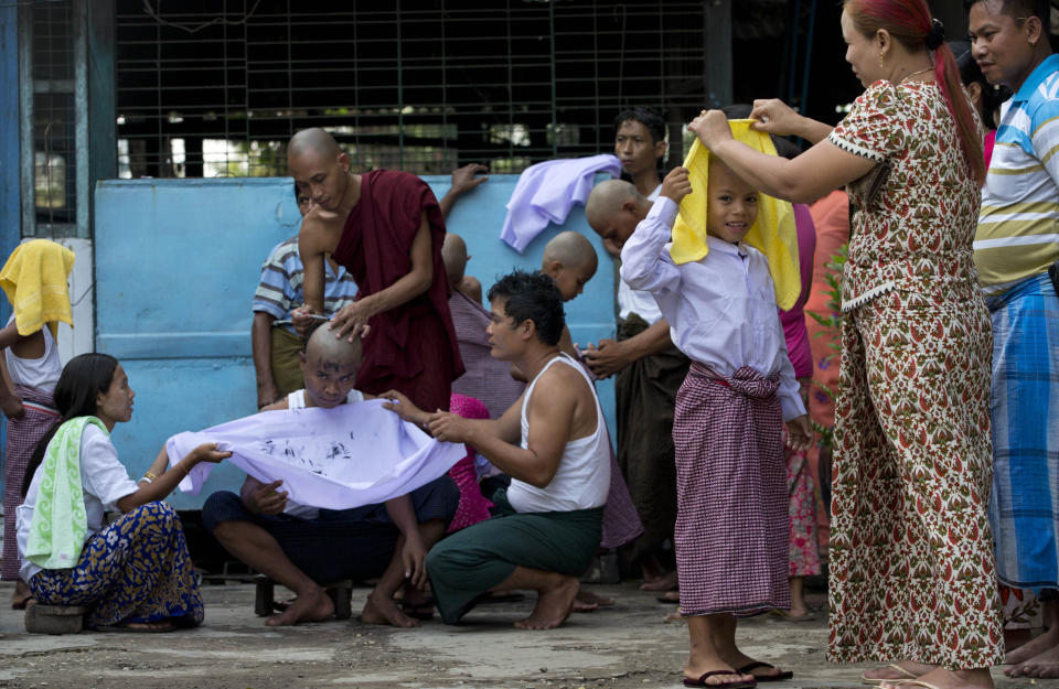 In this April 8, 2014 photo, a boy, right, reveals his newly shaved head to his mother as a Buddhist monk shaves the head of a man during an ordination ceremony at a Buddhist monastery in suburbs of Yangon, Myanmar. Though most boys only remain monks for a few days, ordination is seen as a right of passage in this predominantly Buddhist nation of 60 million. In addition to learning the basic tenants of their faith, it serves as a sort of spiritual credit for their parents, helping emancipate them from a viscous cycle of rebirth and death. (AP Photo/Gemunu Amarasinghe)