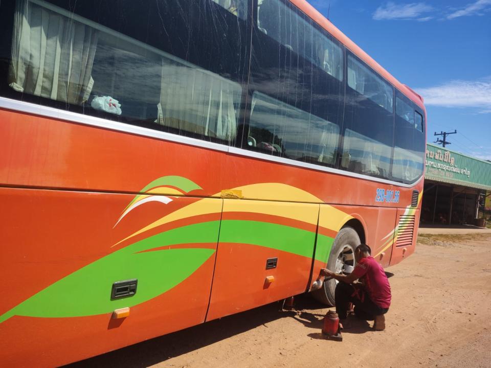 Man helping to repair a broken bus wheel in Laos