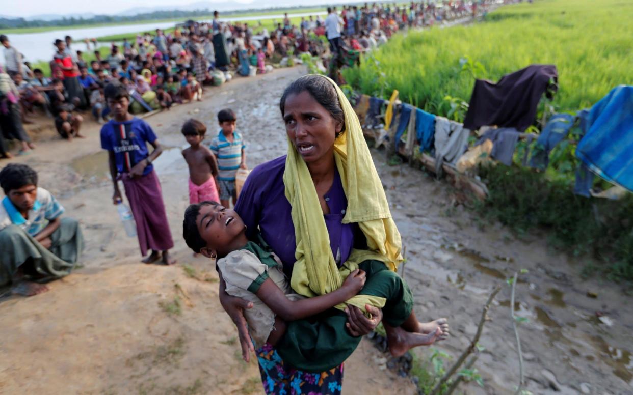 A Rohingya refugee woman who crossed the border from Burma a day before, carries her daughter and searches for help as they wait to receive permission from the Bangladeshi army to continue their way to the refugee camps, in Palang Khali, Bangladesh  - REUTERS