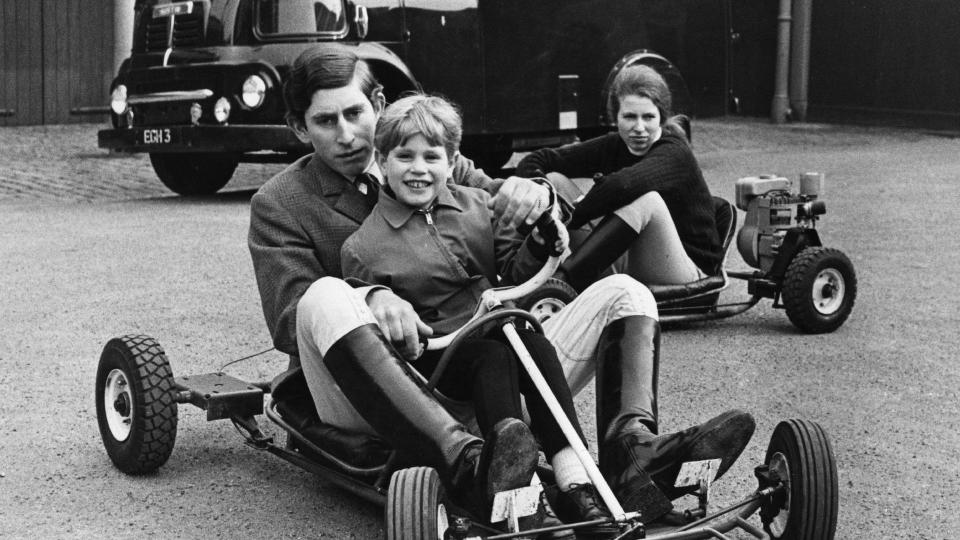 Prince Charles driving a go-kart with Prince Edward on his lap; Princess Anne is in a separate go-kart