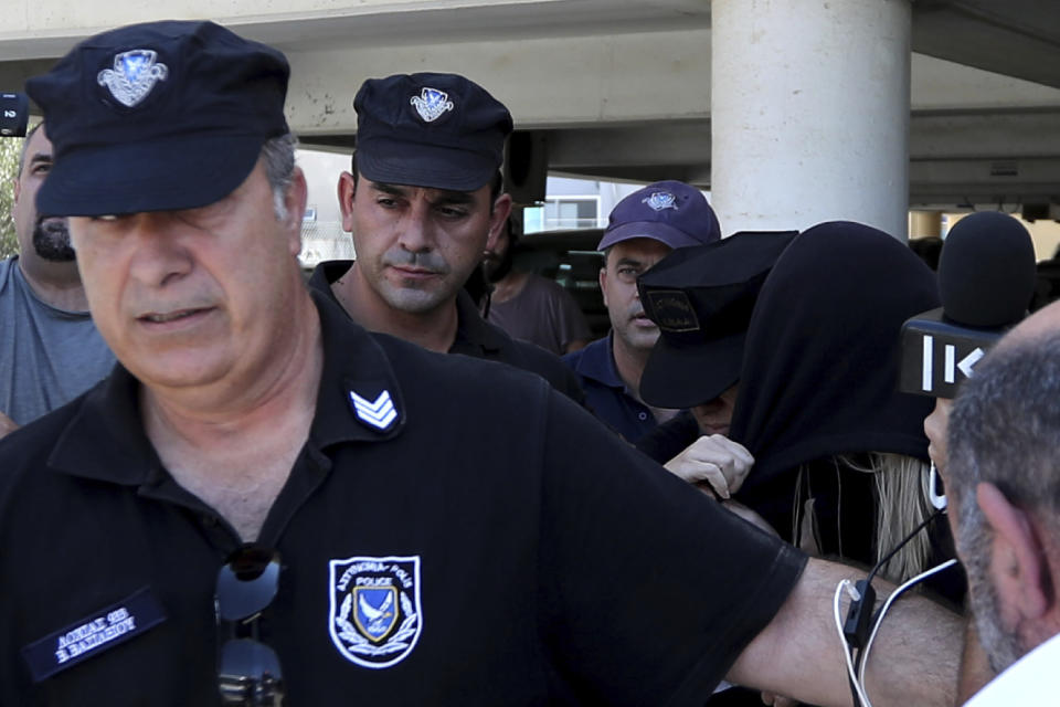 Elite police unit officers escort a 19-year old British woman, center with head covered, to Famagusta court in Paralimni, Cyprus, Tuesday, July 30, 2019. The British woman faces a public nuisance charge after she admitted that her accusation that 12 Israeli teens raped her at a popular resort town was untrue. (AP Photo/Petros Karadjias)