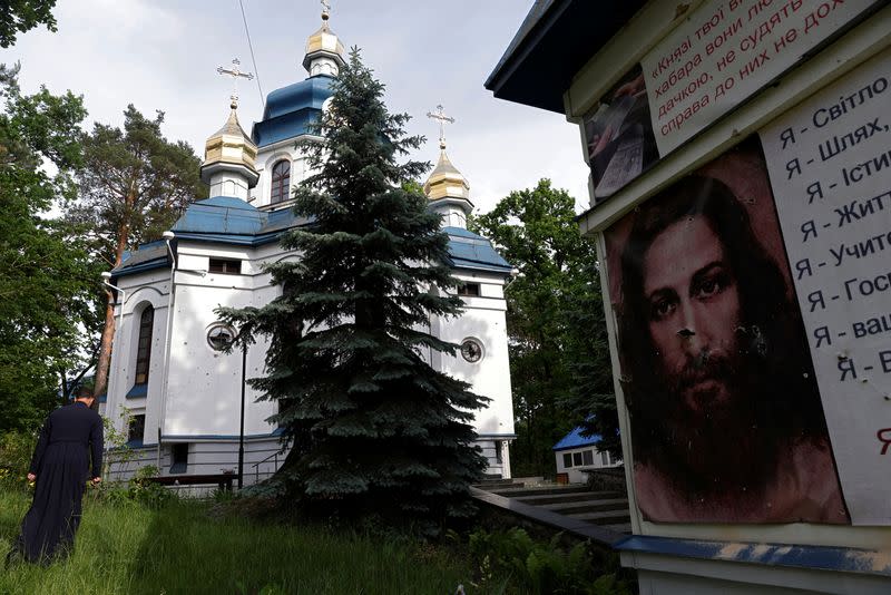 Parish priest Andriy Klyushev passes a damaged poster of Jesus and the damaged Saint Nicholas church, as Russia's attack on Ukraine continues, Irpin