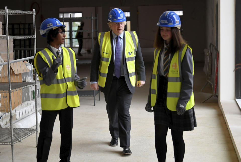 Britain's Prime Minister Boris Johnson talks with year 10 pupils Vedant Jitesh and Eryn Davies during a visit to the construction site of Ealing Fields High School in west London, Monday June 29, 2020. (Toby Melville/Pool via AP)