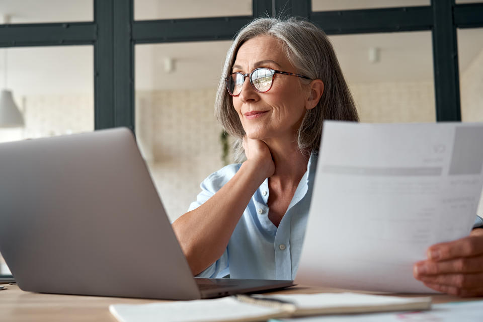 Smiling mature middle aged business woman using laptop working on computer sitting at desk. Happy old businesswoman hr holding cv interviewing distance applicant, senior seeker searching job online.