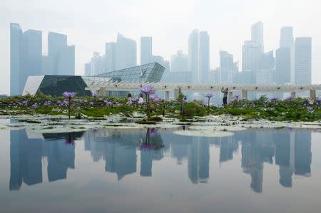 People pass the skyline of Singapore's central business district shrouded by haze August 26, 2016. REUTERS/Edgar Su