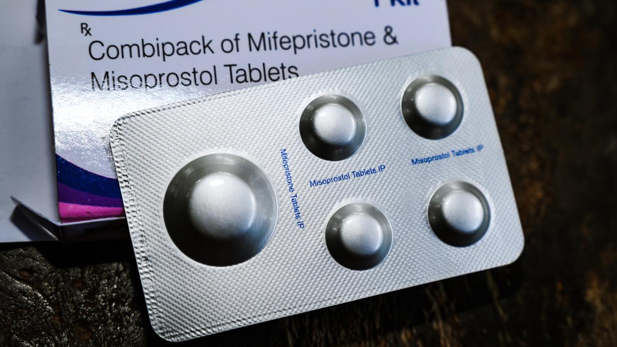  Close-up image of a silver packet of mifepristone and misoprostol pills with the white box behind it. 
