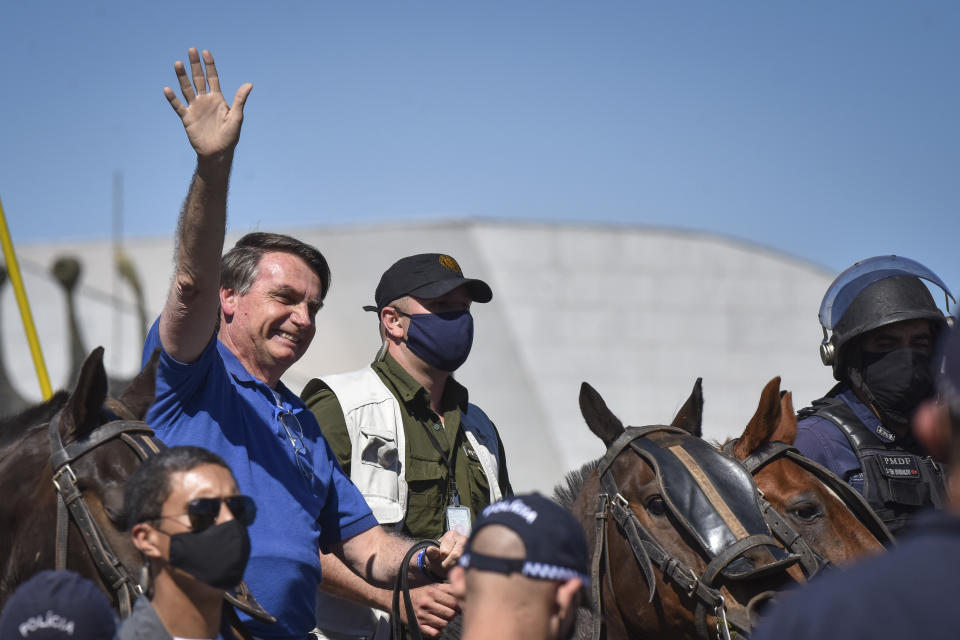 Brazil's President Jair Bolsonaro rides a horse greeting supporters outside the presidential palace in Brasilia, Brazil, Sunday, May 31, 2020. Bolsonaro mounted a horse from police that were guarding supporters of his government gathered outside the Planalto Palace. (AP Photo/Andre Borges)