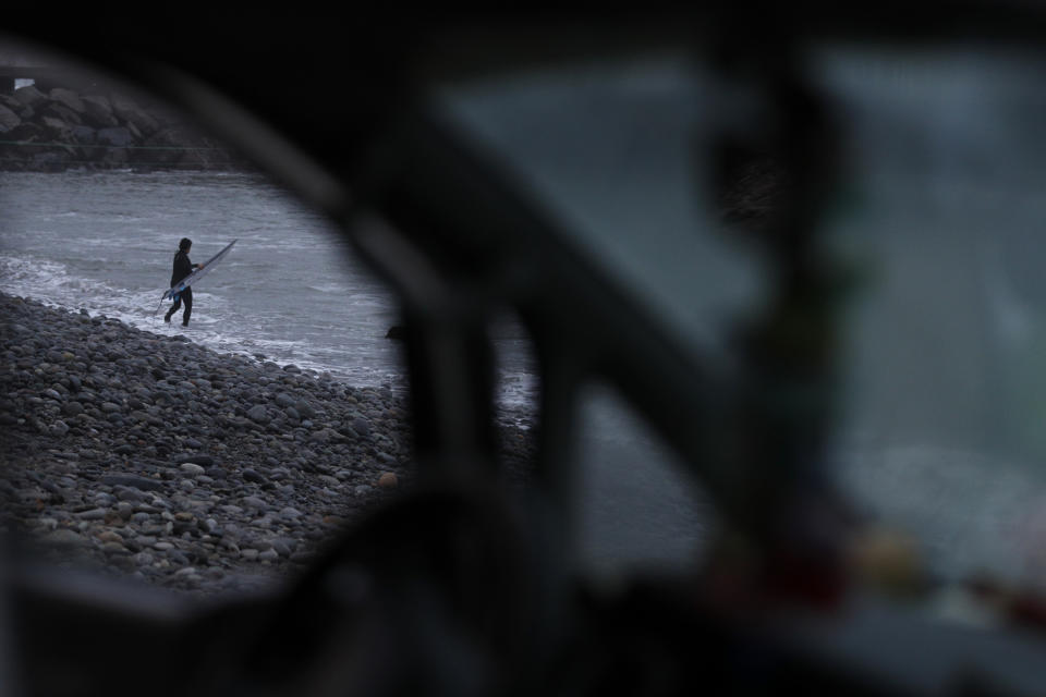 In this July 26, 2019 photo, a surfer is seen through the open window of a surf school van as he heads into the water in the early morning at Makaha beach, Lima, Peru. Surfing is a way of life in Peru, which has been called the Hawaii of Latin America. (AP Photo/Rebecca Blackwell)