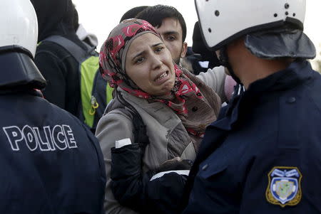 A Syrian refugee woman holding her baby reacts in front of a Greek police cordon while trying to reach a narrow border crossing into Macedonia near to the Greek village of Idomeni December 4, 2015. REUTERS/Yannis Behrakis