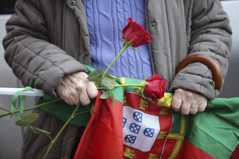 A Socialist Party supporter holds roses and a Portuguese flag during an election campaign action with their leader Pedro Nuno Santos on the street in the Lisbon suburb of Moscavide, Friday, March 8, 2024. Portugal is holding an early general election on Sunday when 10.8 million registered voters elect 230 lawmakers to the National Assembly, the country's Parliament. (AP Photo/Joao Henriques)