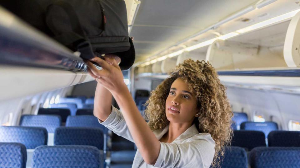 Young businesswoman places carry on in airline bin