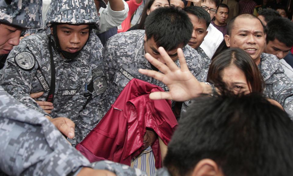 Andal Ampatuan Sr., center, a powerful Filipino clan leader who is a suspect in the 2009 massacre of 57 people, covers his face as he is escorted under tight security following his arraignment in Pasay city, south of Manila, Philippines on Monday March 26, 2012. Andal Sr. has been on trial for murder and on Monday pleaded not guilty to charges of rigging elections to favor former President Gloria Macapagal Arroyo's allies. (AP Photo/Aaron Favila)