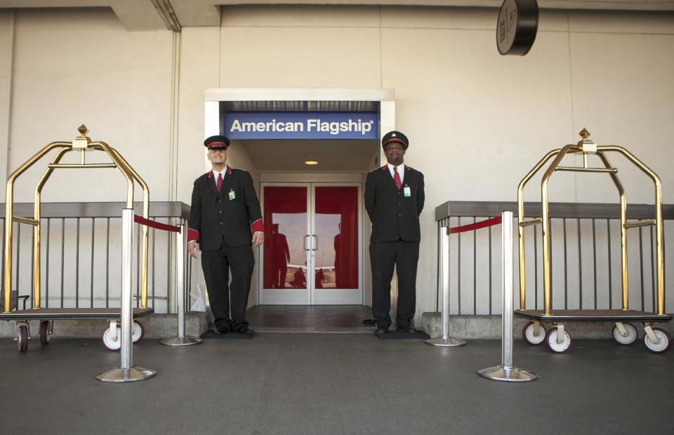 In this Thursday, March 14, 2013 photo, American Airlines skycaps Alex Abel Gonzalez, left, and Frederick Pearson await outside the AA Flagship lounge at Los Angeles International Airport, LAX. American's Flagship Check-in service, a VIP discreet and expedited check-in process offers personal access to agents for assistance with check-in and bag check, and a separate security line when flying through LAX and now Miami International Airport. (AP Photo/Damian Dovarganes)