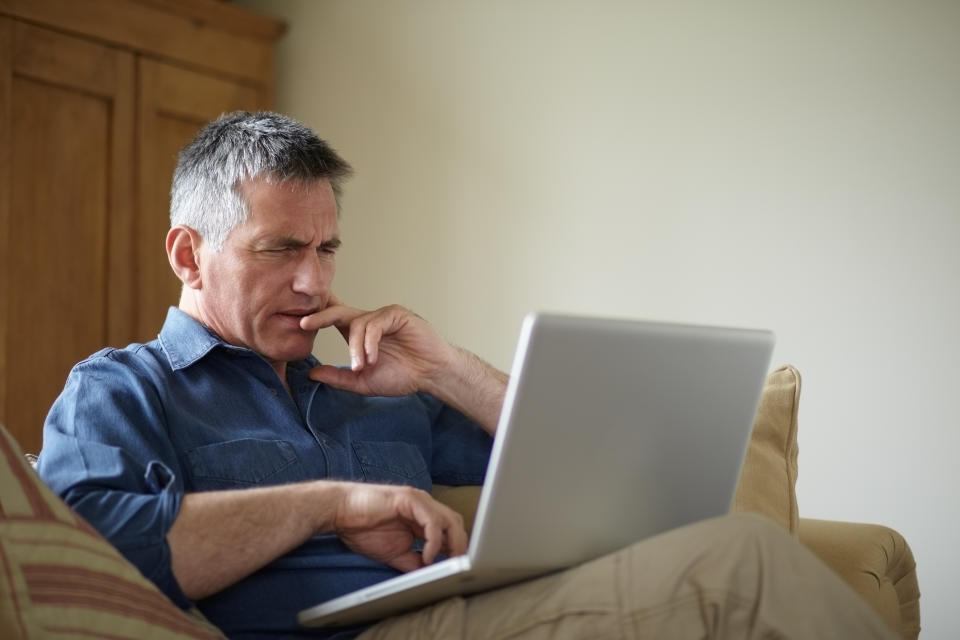 A man sits on a couch looking at his laptop. Lottery agents provide information on past winning numbers.
