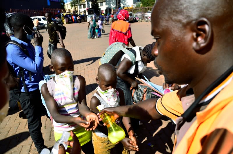 A man puts hand sanitizer on passengers hands before boarding public transport buses as residents leave for the villages amid concerns over the spread of coronavirus disease (COVID-19) at a bus terminal in Old Kampala