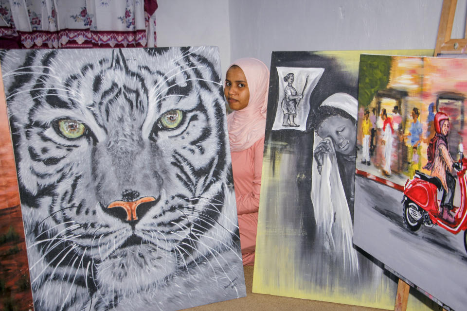 Somali artist Sana Ashraf Sharif Muhsin, 21, sits with some of her paintings at her home in the capital Mogadishu, Somalia Friday, Oct. 15, 2021. Among the once-taboo professions emerging from Somalia's decades of conflict and Islamic extremism is the world of arts, and this 21-year-old female painter has faced more opposition than most. (AP Photo/Farah Abdi Warsameh)