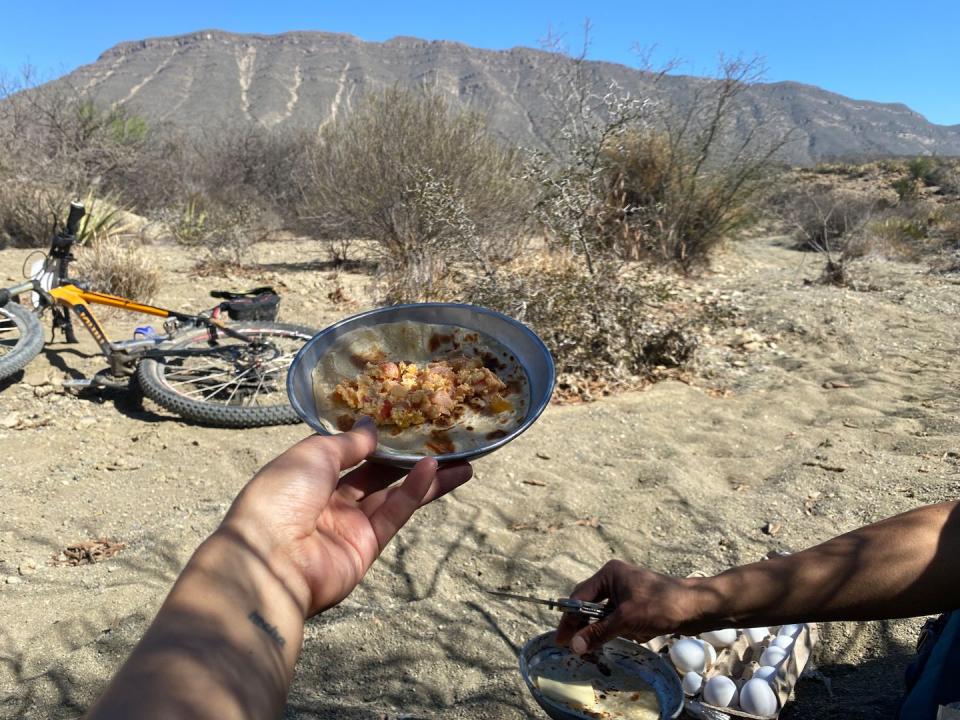 a person holds out a plate with a breakfast taco against a desert background