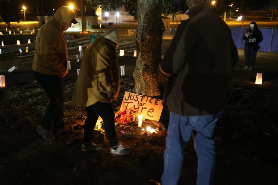 Por la noche, tres personas con abrigos observan un cartel apoyado en un árbol e iluminado con velas. Se lee: ‘Justicia para Tyre’. <a href="https://www.gettyimages.com/detail/news-photo/people-attend-a-candlelight-vigil-in-memory-of-tyre-nichols-news-photo/1459866296?phrase=tyre%20nichols&adppopup=true" rel="nofollow noopener" target="_blank" data-ylk="slk:Scott Olson/Getty Images News via Getty Images;elm:context_link;itc:0;sec:content-canvas" class="link ">Scott Olson/Getty Images News via Getty Images</a>