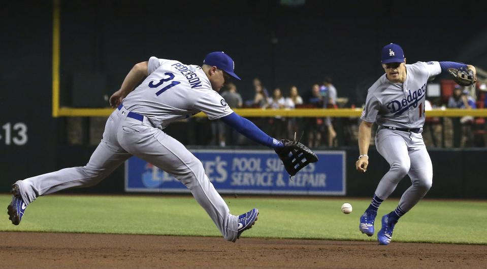 Los Angeles Dodgers first baseman Joc Pederson (31) makes an error on a grounder hit by Arizona Diamondbacks' David Peralta as Dodgers second baseman Enrique Hernandez, right, moves in to help out during the first inning of a baseball game Wednesday, June 26, 2019, in Phoenix. (AP Photo/Ross D. Franklin)