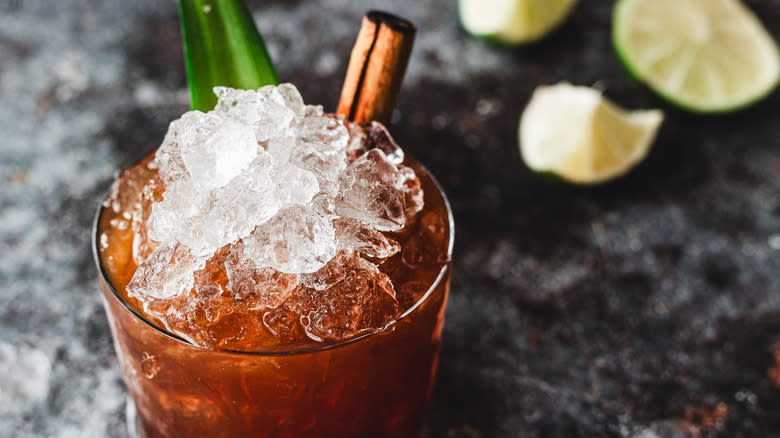 Red cocktail with ice and pineapple leaf, limes in back