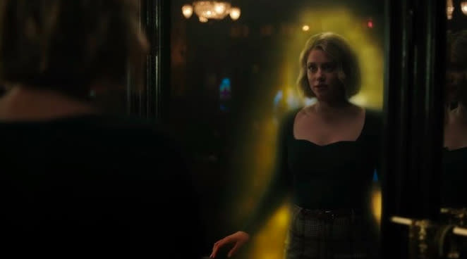 Betty, a young woman with a blonde bob, looks at herself in the mirror. She is surrounded by a glowing yellow aura.