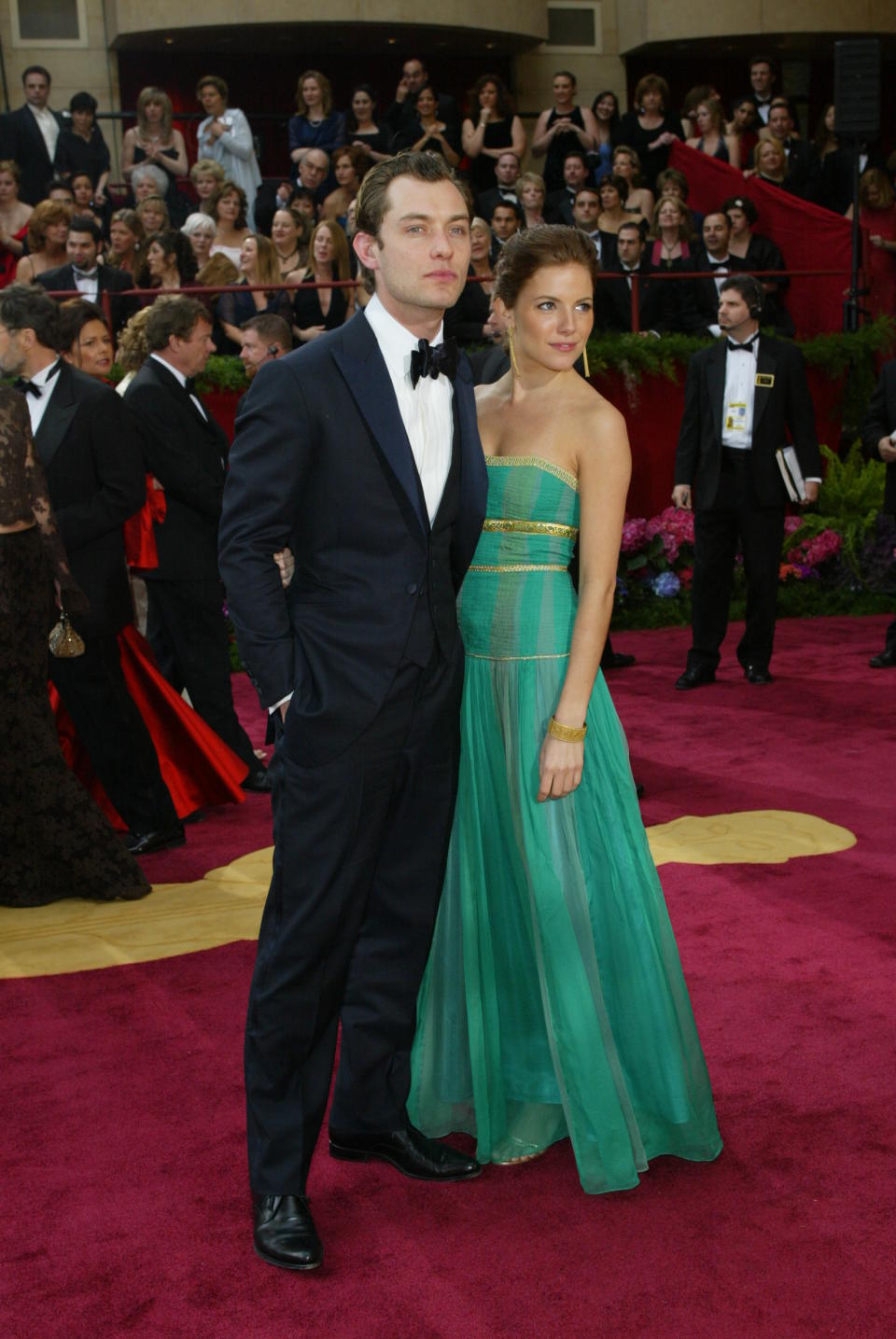 Jude Law in a tuxedo and Sienna Miller in a green dress at the Oscars. 