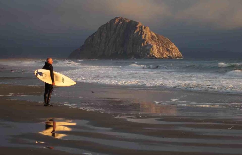 A surfer stands at the edge of the water. 