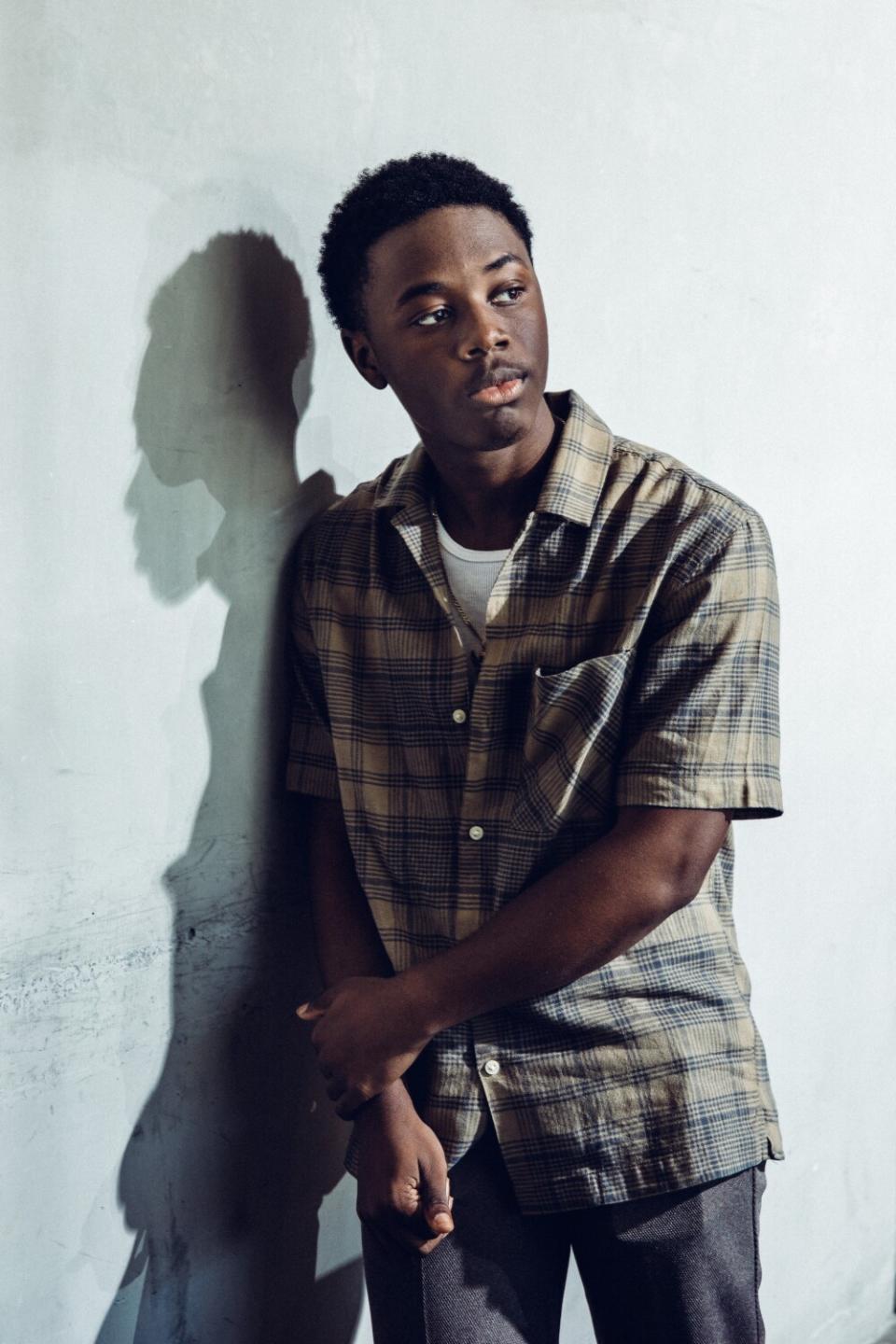 A teen actor leans on a white wall