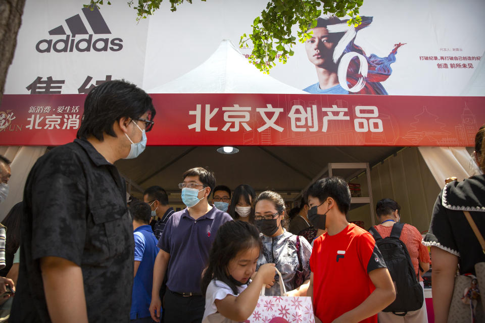 People wearing face masks to protect against the new coronavirus browse merchant tents at a government event aiming to stimulate consumer demand and consumption in Beijing, Saturday, June 6, 2020. China's capital is lowering its emergency response level to the second-lowest starting Saturday for the coronavirus pandemic. That will lift most restrictions on people traveling to Beijing from Wuhan and surrounding Hubei province, where the virus first appeared late last year. (AP Photo/Mark Schiefelbein)