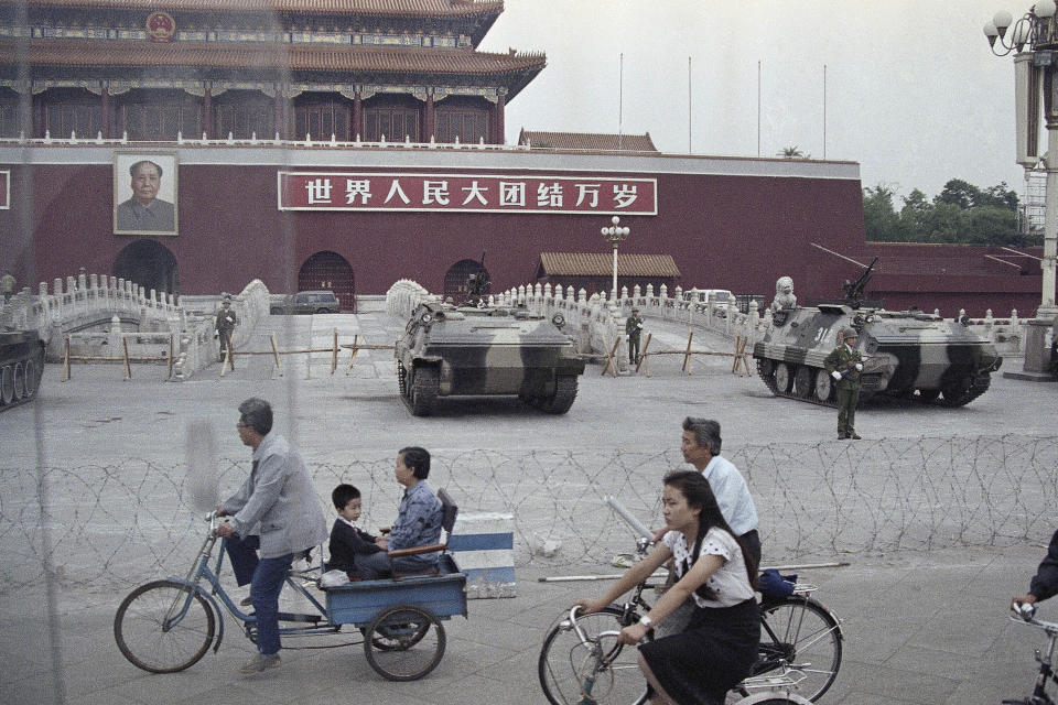 FILE - Cyclists pass by armored vehicles parked in front of Tiananmen Gate near the square where students rallied for democratic reforms in Beijing, June 13, 1989. An exhibit will open Friday, June 2, 2023, in New York, ahead of the June 4 anniversary of the violence that ended China's 1989 Tiananmen protests. (AP Photo/Sadayuki Mikami, File)