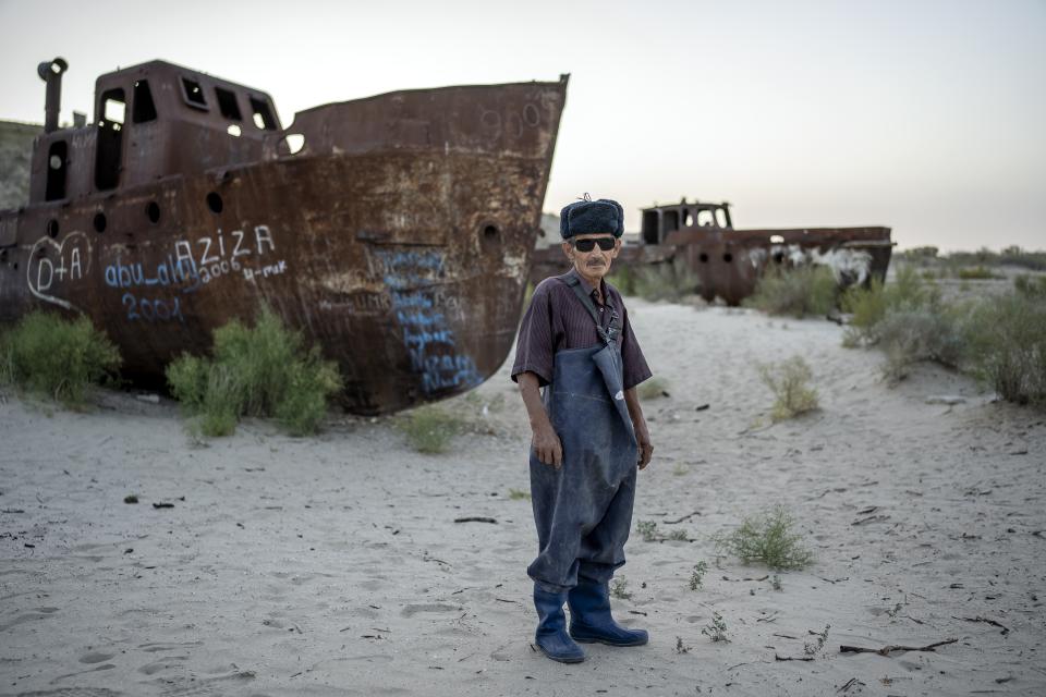 Jowad Khan poses for a photo in front of an old boat in the area where the Aral Sea once was in Muynak, Uzbekistan, Thursday, July 13, 2023. (AP Photo/Ebrahim Noroozi)