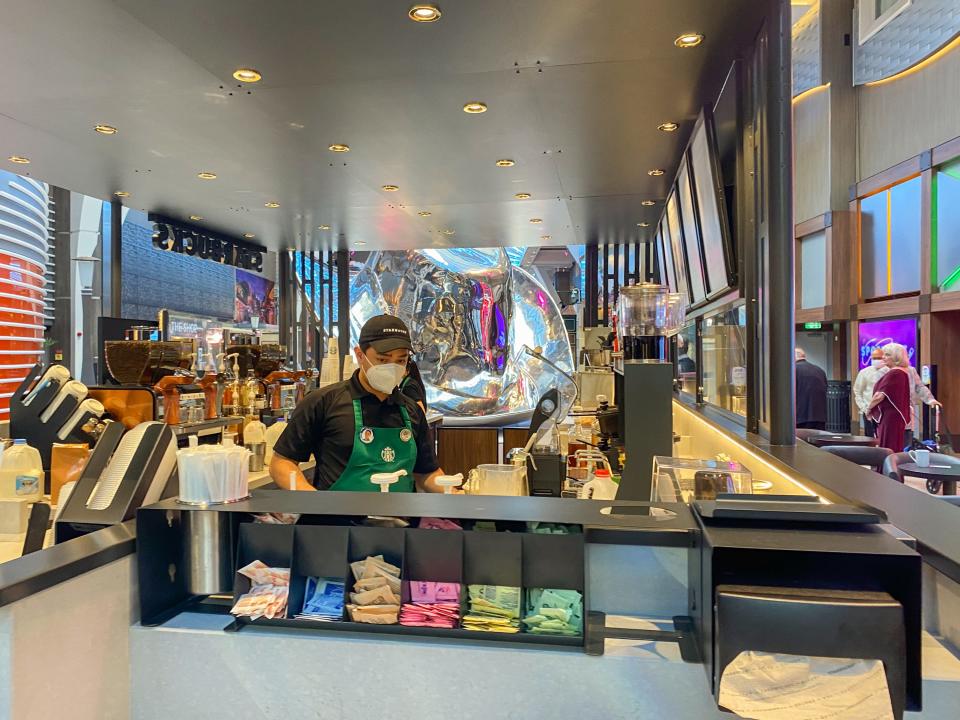 An employee behind a counter at a starbucks stand on an indoor deck on a cruise ship