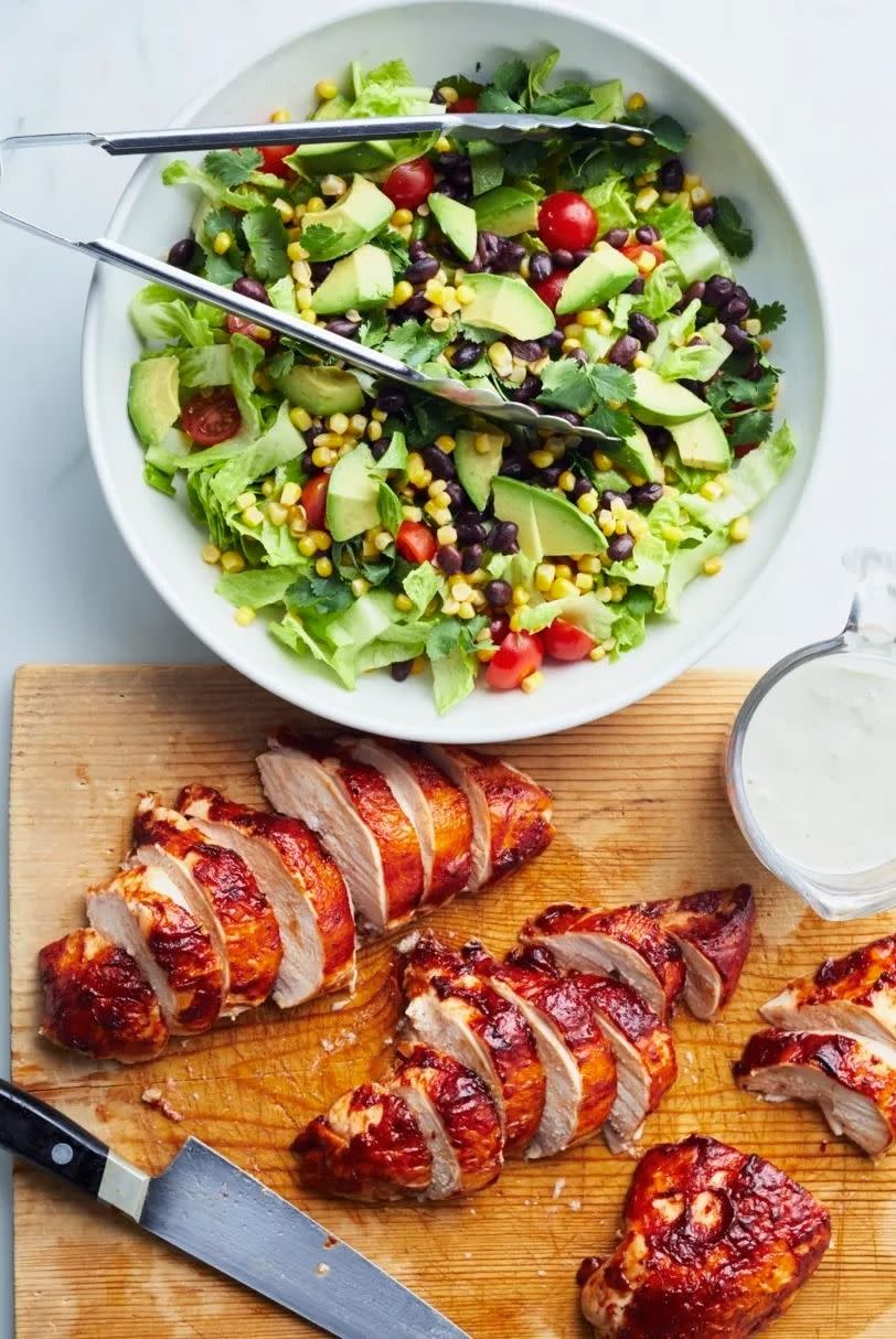 barbecue chicken salad with salad in big white bowl and chicken sliced on cutting board