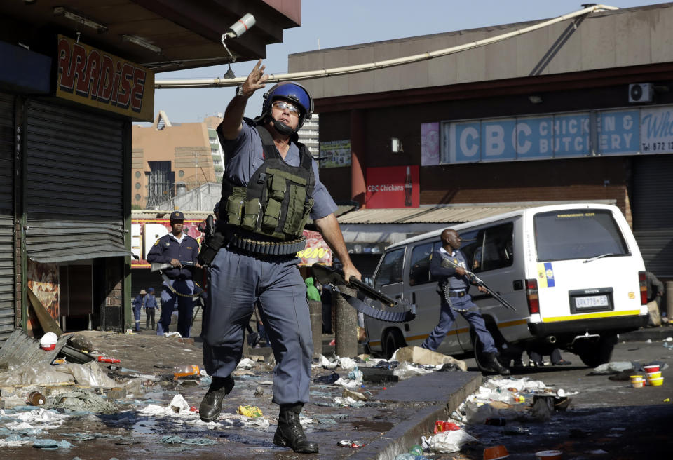 A riot police officer throws a teargas canister as looters make off with goods from a store in Germiston, east of Johannesburg, South Africa, Tuesday, Sept. 3, 2019. Police had earlier fired rubber bullets as they struggled to stop looters who targeted businesses as unrest broke out in several spots in and around the city. (AP Photo/Themba Hadebe)