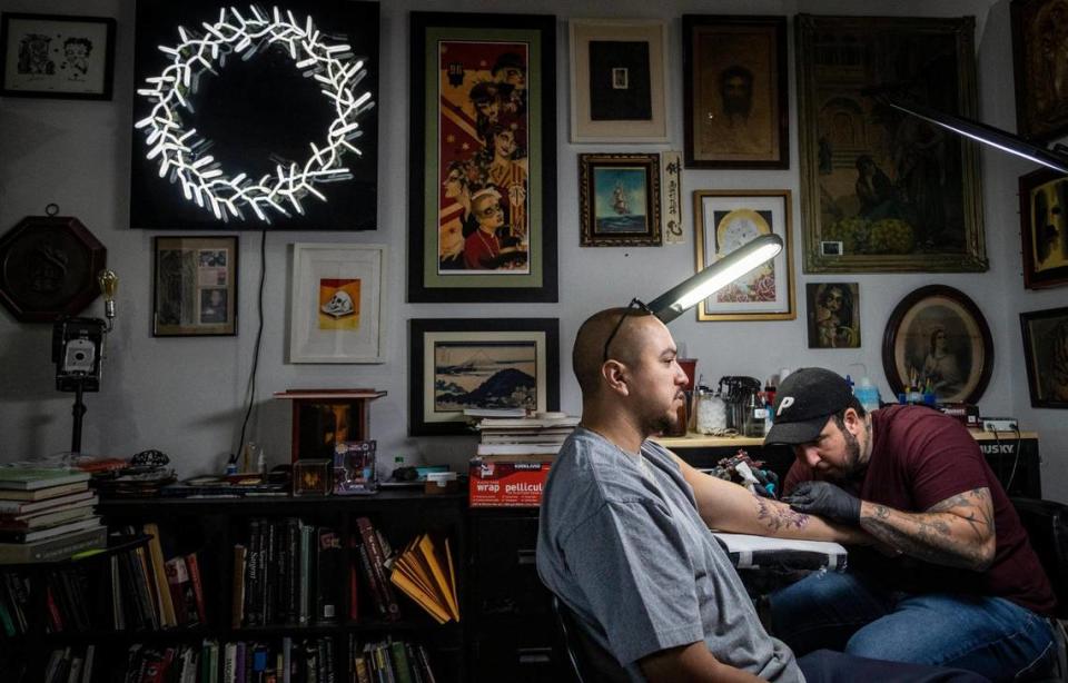 Javier Betancourt, a la derecha, trabaja en una pieza en su estudio de tatuajes de Ocho Placas, que combinó con su White Rose Coffee Shop.