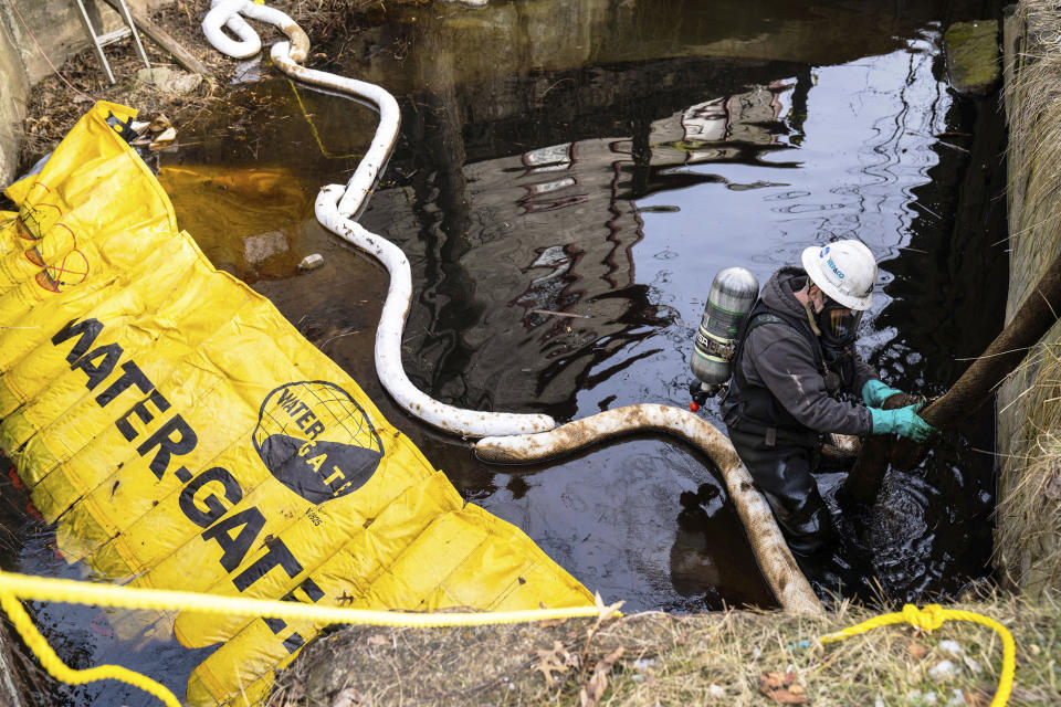 An employee of HEPACO works in a creek along Sumner Street in downtown East Palestine, Ohio, on Sunday, Feb. 5, 2023. A smoldering tangle of dozens of derailed freight cars, some carrying hazardous materials, has kept an evacuation order in effect in Ohio near the Pennsylvania state line as environmental authorities warily watch air quality monitors. (Lucy Schaly/Pittsburgh Post-Gazette via AP)