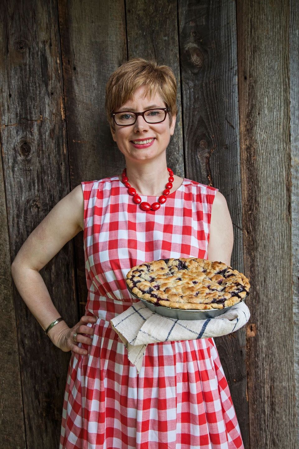a woman in a red gingham dress holding a blueberry crumb pie