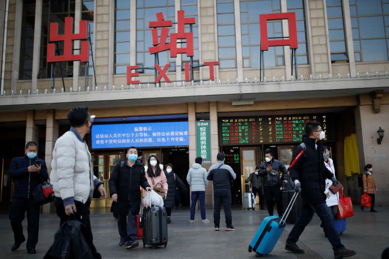 People wearing face masks carry their luggage outside Beijing Railway Station as the country is hit by an outbreak of the new coronavirus, in Beijing