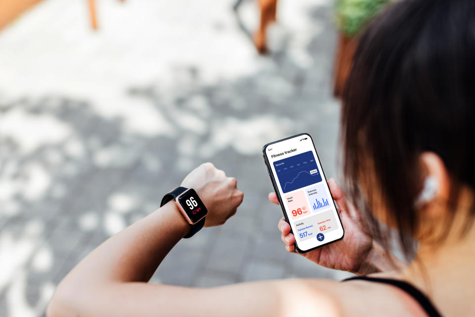 Over the shoulder view of young woman using workout app on smart watch and smartphone to track pace and time. 