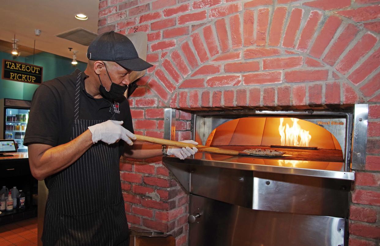 Having finished preparing the dough, The Well restaurant in Randolph co-owner Mark Thompson places the jerk chicken pizza into the fire brick oven for baking on Monday, March 7, 2022.