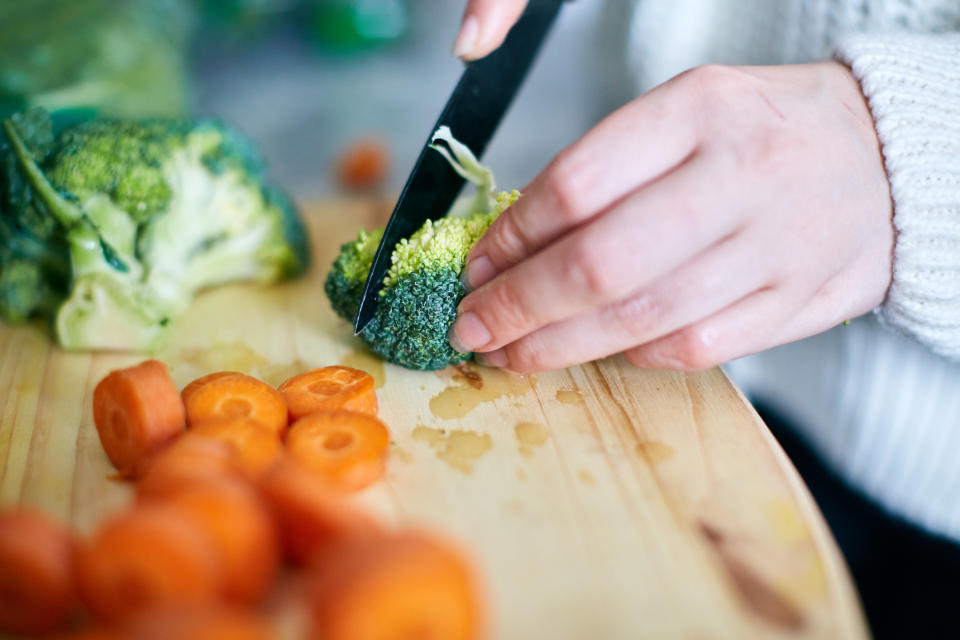 Woman's hand slicing broccoli on wooden chopping board.