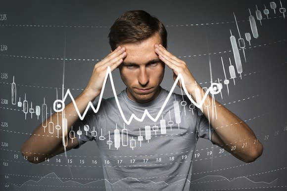 Man holding hands on forehead as in deep thought behind image of stock chart going up