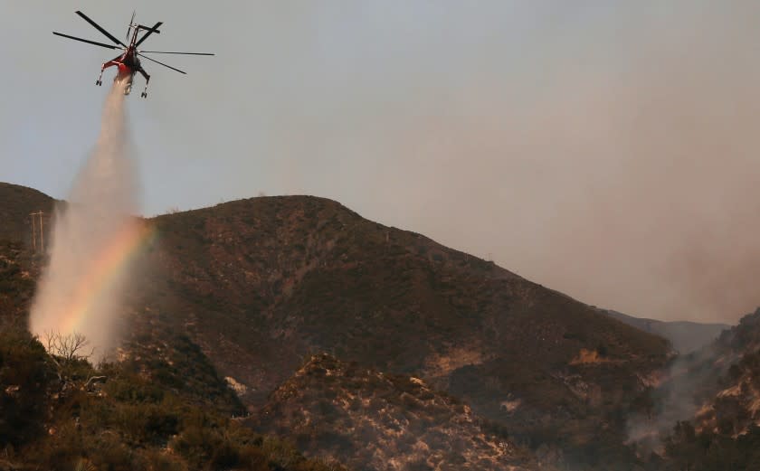 PASADENA, CALIFORNIA - SEPTEMBER 23: A firefighting helicopter makes a water drop, as a rainbow appears in the mist, during the Bobcat Fire in the Angeles National Forest on September 23, 2020 near Pasadena, California. The Bobcat Fire, burning in the San Gabriel Mountains, has grown to over 113,000 acres with containment jumping to 38 percent. (Photo by Mario Tama/Getty Images)