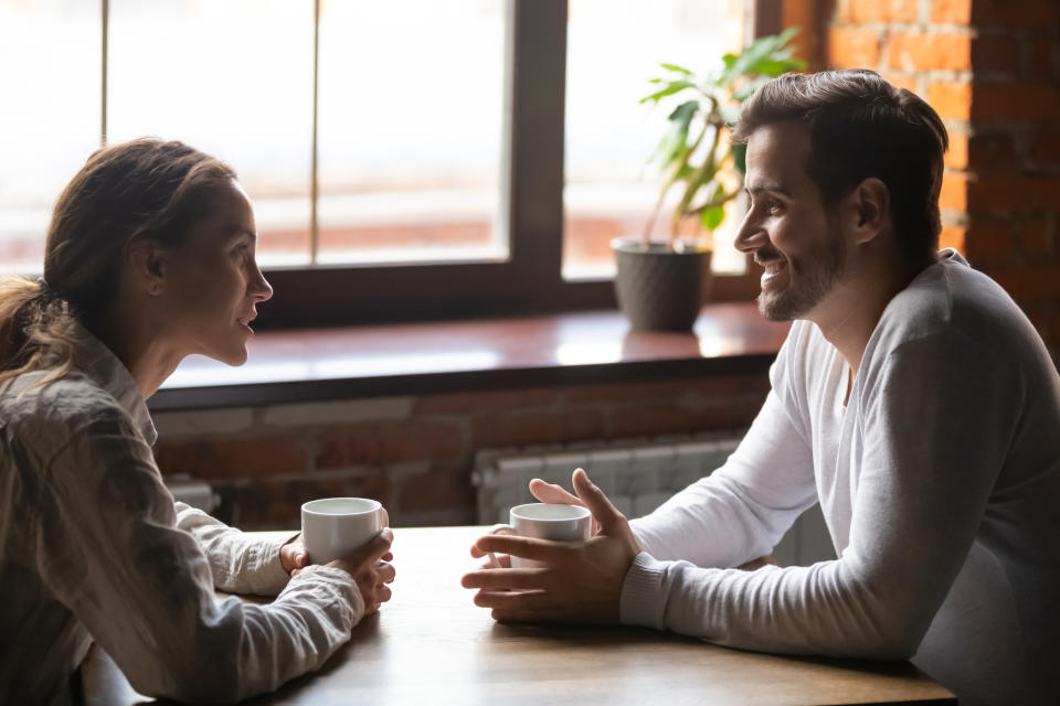 Side view smiling biracial woman sitting at table in cafe with caucasian man couple talking in cozy coffeeshop drinking tea coffee. Heterosexual friends romantic relationships or speed dating concept