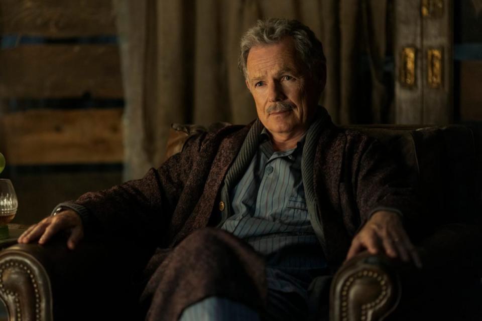 Bruce Greenwood with a mustache sits in a chair in pjs in The Fall Of The House Of Usher