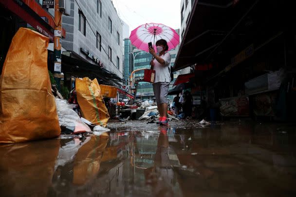 PHOTO: A woman using an umbrella takes photographs of a road that was flooded after torrential rain, at a traditional market in Seoul, South Korea, on Aug. 9, 2022. (Kim Hong-ji/Reuters)