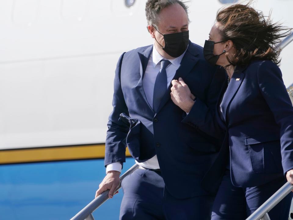 Kamala Harris and Doug Emhoff exit Air Force Two arm in arm, smiling at each other.