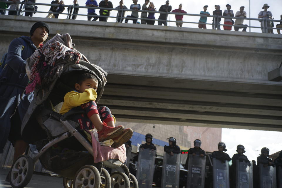 A migrant man pushes a child in a baby stroller past a cordon of riot police as he joins a small group of migrants trying to cross the border together at the Chaparral border crossing in Tijuana, Mexico, Thursday, Nov. 22, 2018. A small group of Central American migrants marched peacefully to a border crossing in Tijuana Thursday to demand better conditions and push to enter the U.S. (AP Photo/Ramon Espinosa)