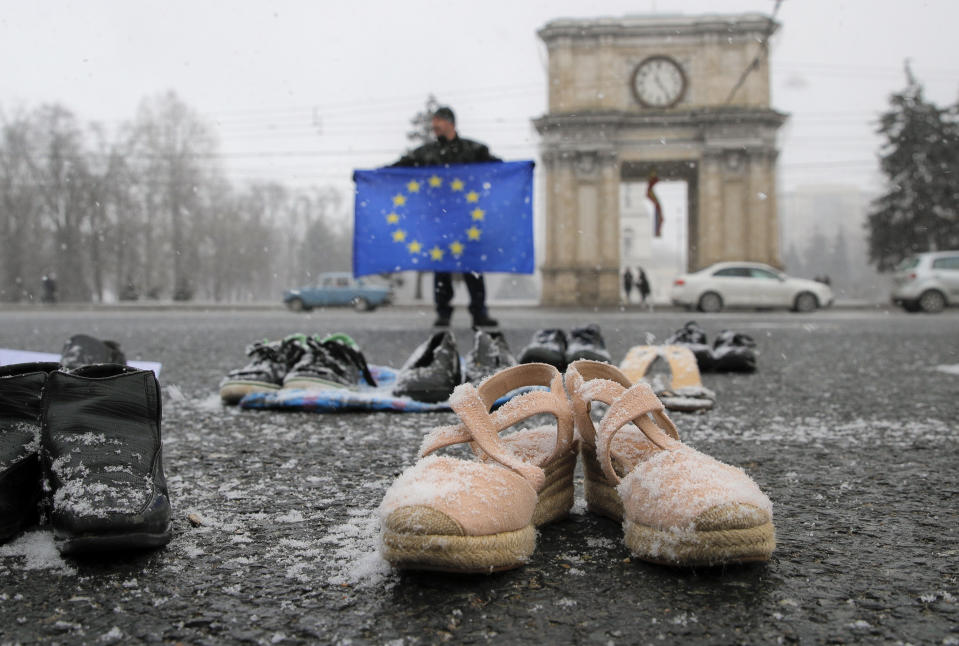 FILE - In this Saturday, Feb. 23, 2019 file photo, a man holds a European Union flag as people stand by shoes of Moldovan citizens working abroad are placed on the pavement in Chisinau, Moldova. A Moldovan court has appointed former prime minister Pavel Filip as interim president, a day after a new government was formed following a months-long political stalemate. The Constitutional Court said Sunday, June 9 that Igor Dodon, who supported the new government, was being relieved of his duties for failing to comply with its ruling to dissolve parliament. (AP Photo/Vadim Ghirda, file)